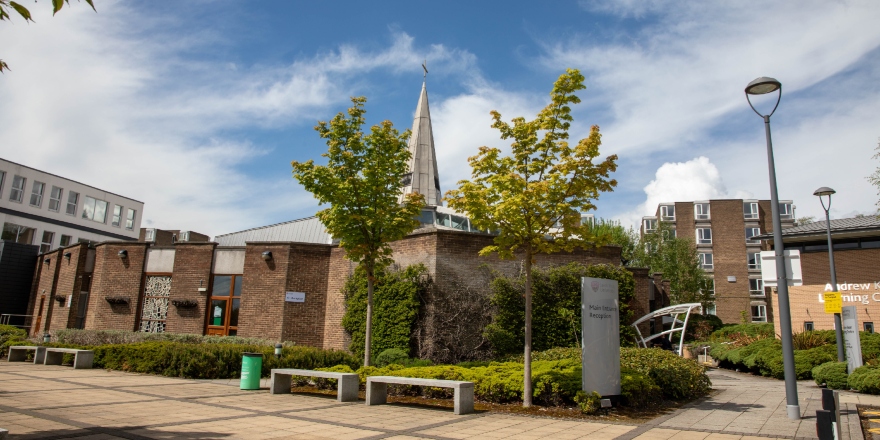 An exterior image of the Leeds Trinity University Chapel, behind two green trees.