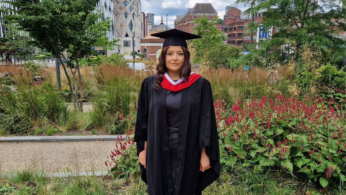 A girl with dark hair wearing a black cap and gown smiles for a picture