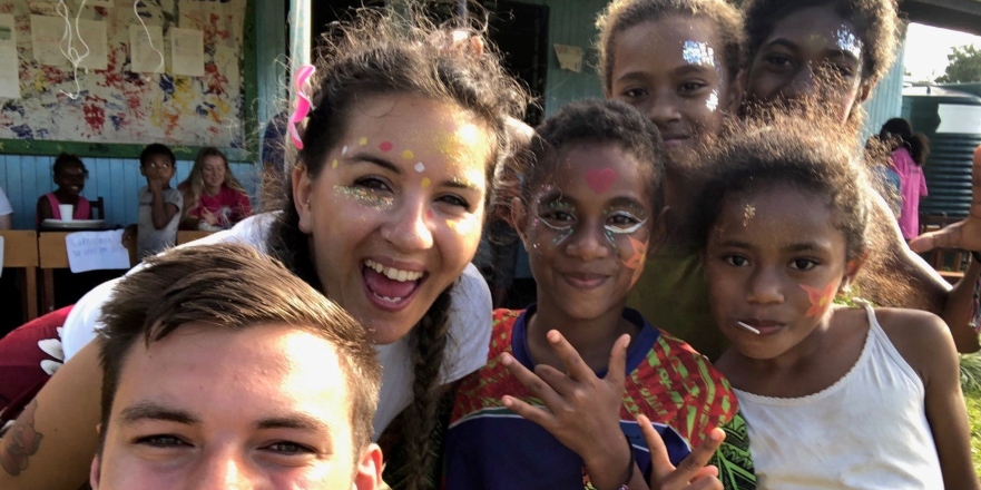 Female student brown hair with school children in Fiji wearing glitter.