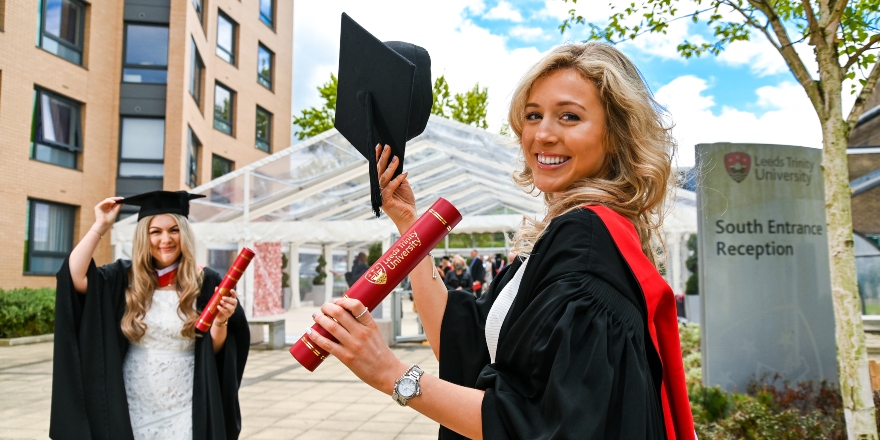 Students wearing gowns and holding certificate tubes on Leeds Trinity campus.