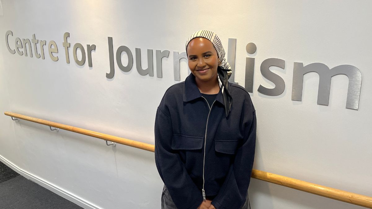 A student stands in front of a white wall displaying the words Centre for Journalism