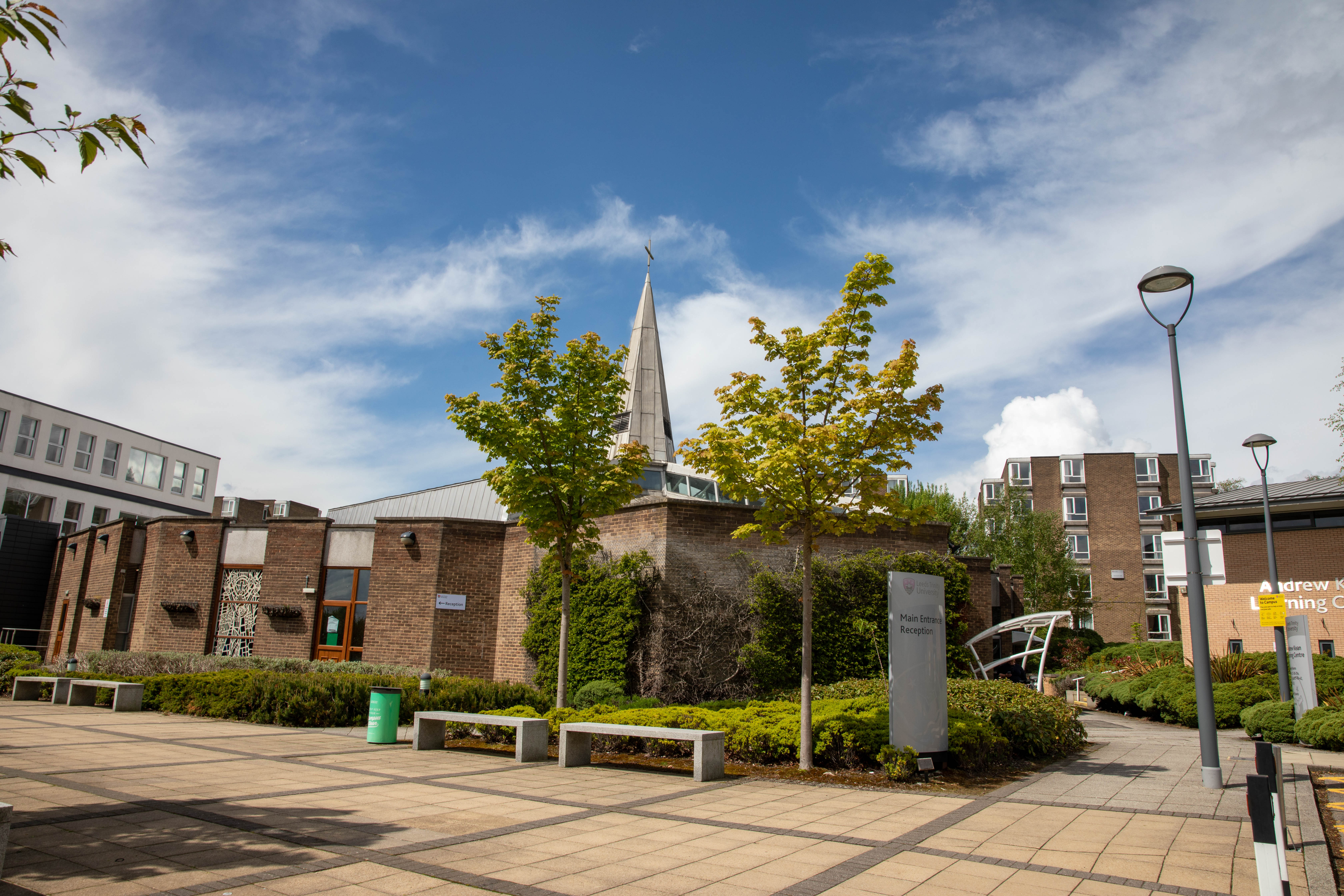 Exterior shot of Leeds Trinity University Chapel on its campus in Horsforth, with green trees and signage in the forefront