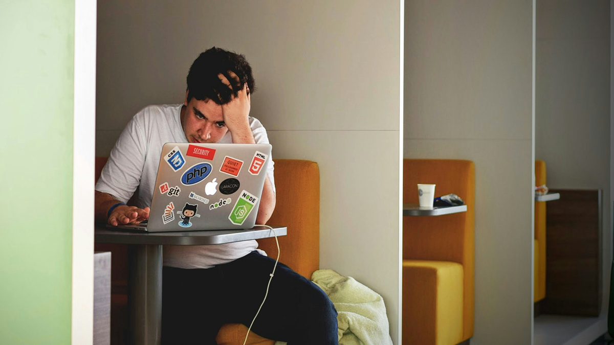 A student working on a laptop with his head rested on his arm.